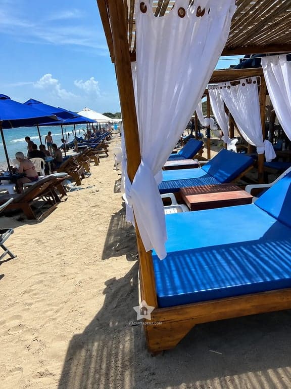 Fila de camas con dosel y cortinas blancas junto a la orilla en Playa Linda, Tierra Bomba
