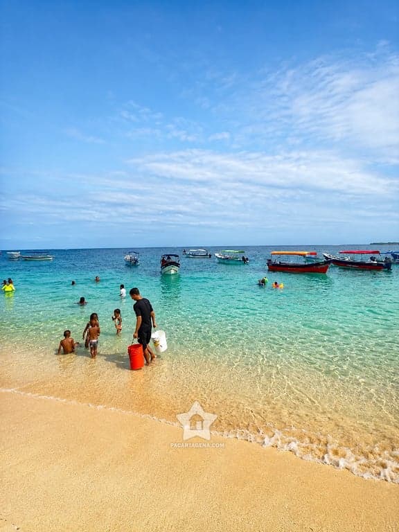 Aguas cristalinas y arena clara en Playa Blanca, Barú, con lanchas y bañistas
