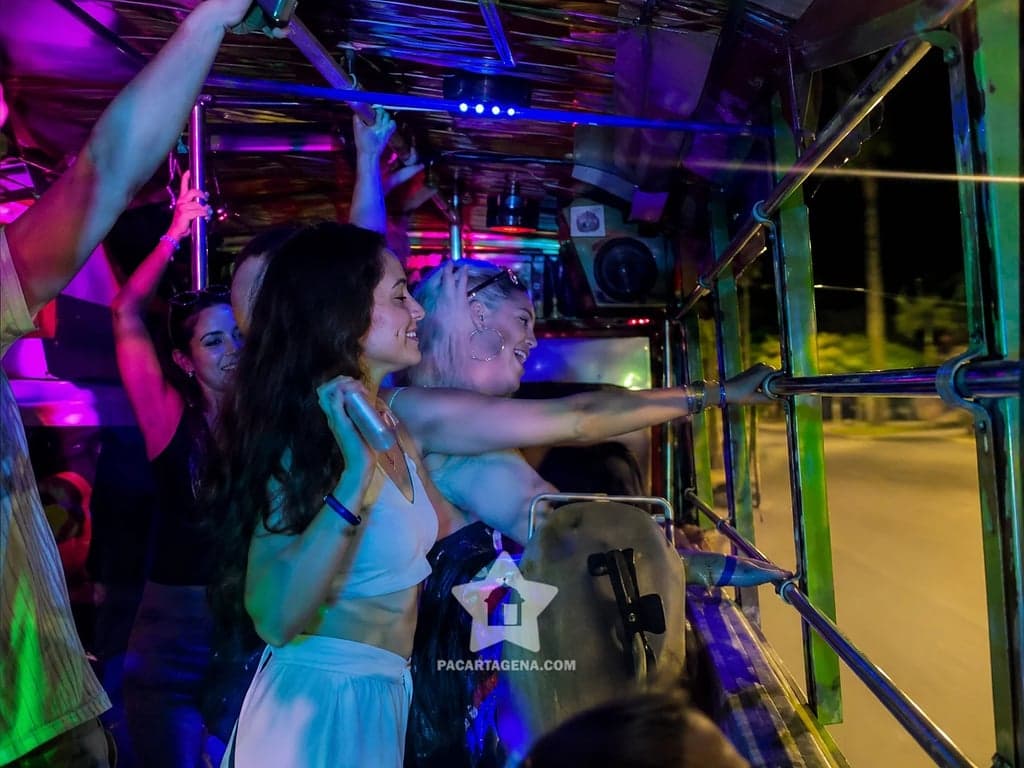 Amigas asomadas y sonrientes en la chiva rumbera mientras recorre Cartagena de noche