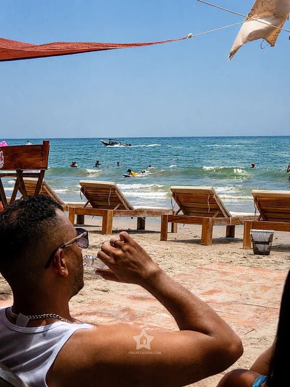 Visitante con un trago frente a los camastros y el mar de Playa Linda, Tierra Bomba