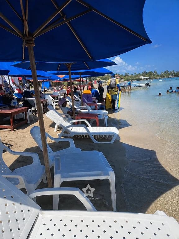 Camastros blancos bajo sombrillas azules en la arena de Playa Linda, Tierra Bomba