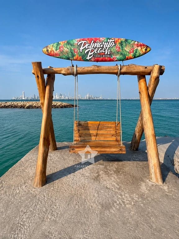 Columpio de madera con el letrero de Palmarito Beach frente al mar y el perfil de Cartagena