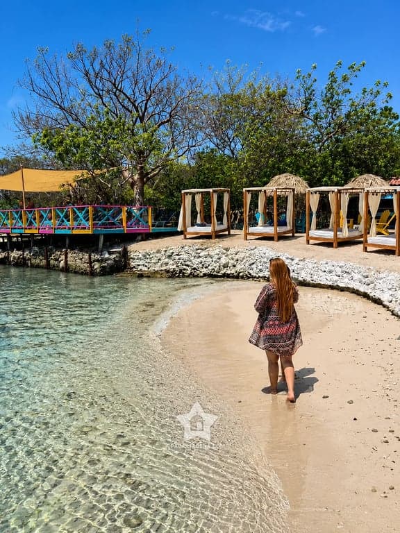 Orilla de arena y aguas cristalinas en una isla del Rosario, con camas de descanso al fondo