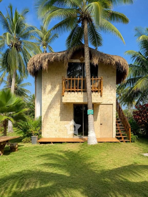 Cabaña de techo de palma entre palmeras y jardín, en Palmarito Beach Club