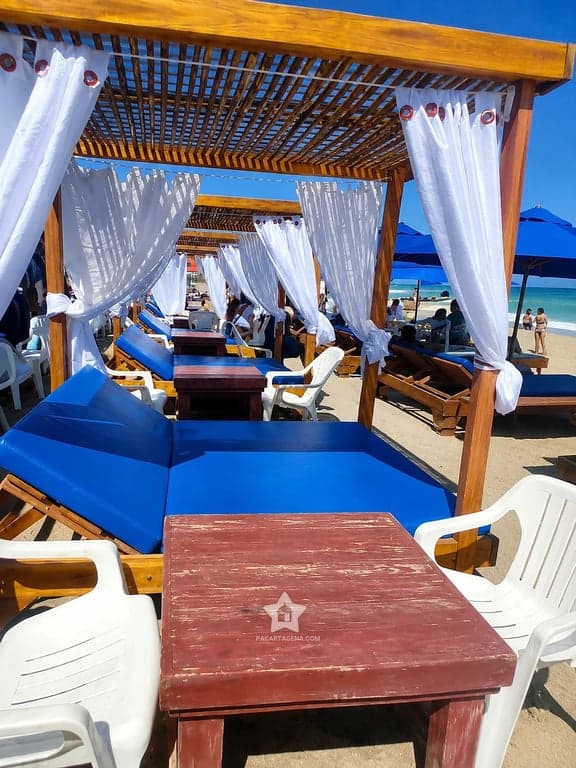 Camas con colchoneta, mesa y sillas en la zona de descanso de Playa Linda, Tierra Bomba