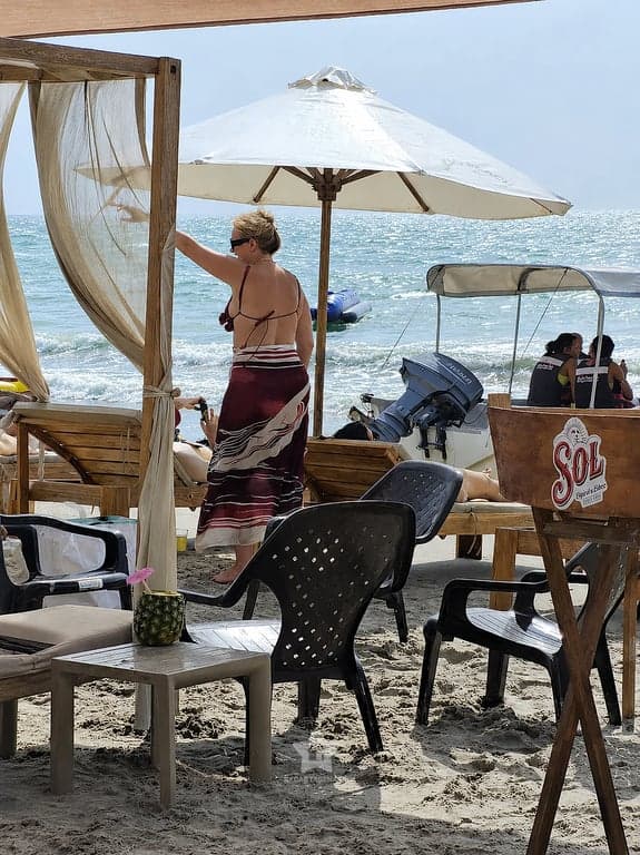 Mesa con cóctel en piña bajo sombrilla, frente al mar de Playa Linda en Tierra Bomba