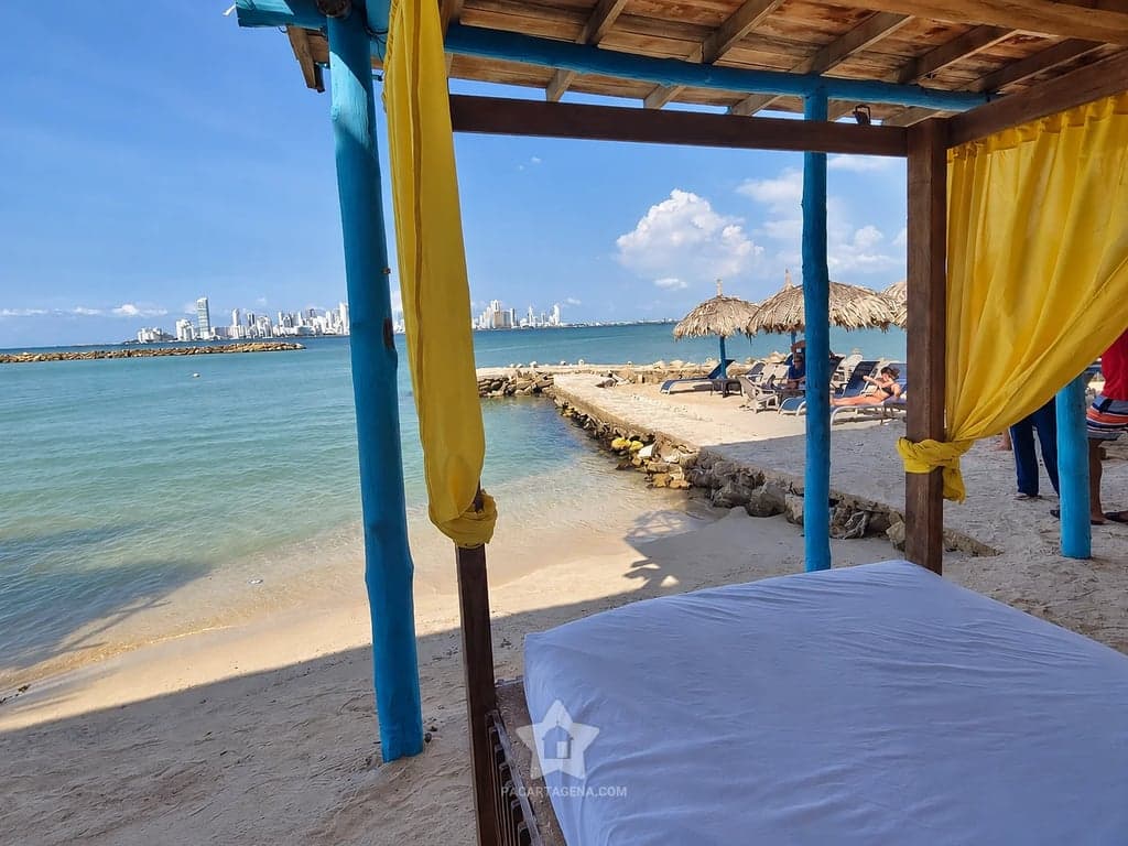 Cama con cortinas amarillas junto a la orilla, con vista a la bahía de Cartagena