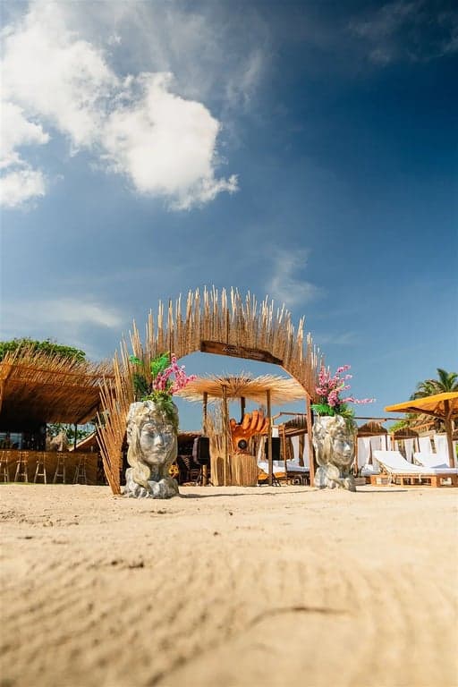 Entrada de madera de Ancestral Lounge y zona de camas de playa bajo sombrillas