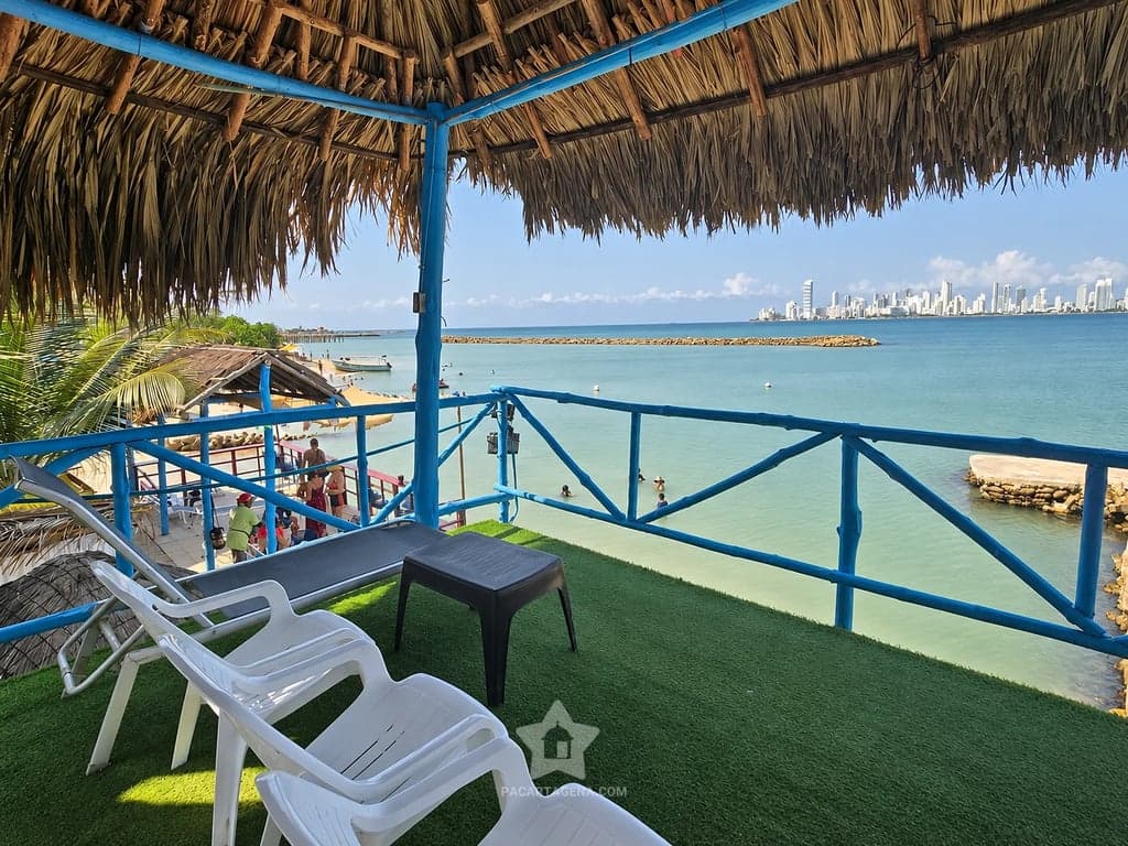 Terraza del segundo piso con sillas blancas y baranda azul, frente a la bahía y a Cartagena