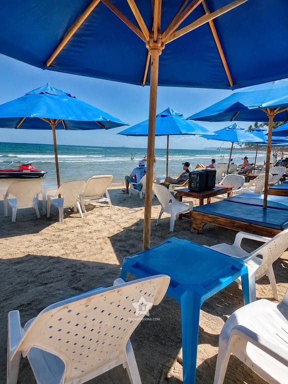 Mesa y sillas bajo sombrilla azul en Playa Linda, con el mar de Tierra Bomba al fondo