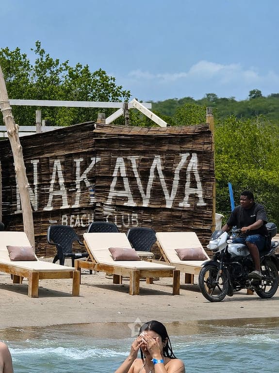 Letrero de madera de Nakawa Beach Club junto a los camastros, al borde del agua en Playa Linda