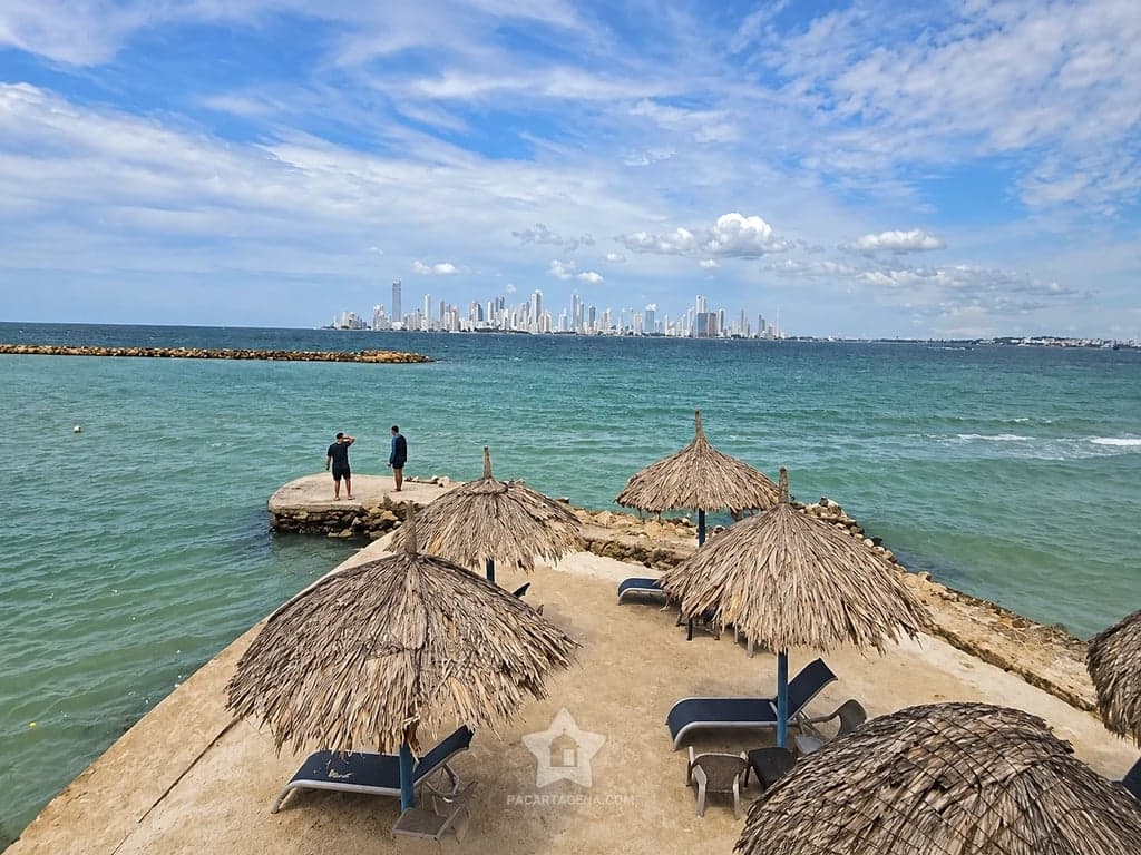 Bohíos y tumbonas sobre el espolón de piedra, con Cartagena al otro lado de la bahía
