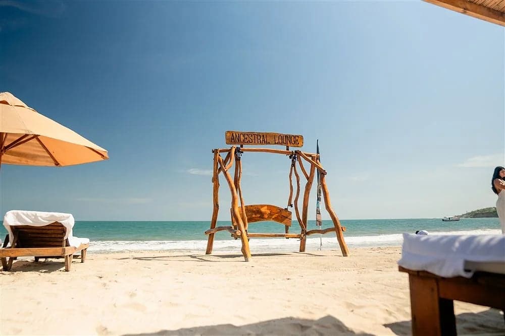 Columpio de Ancestral Lounge frente al mar, con asoleadoras y sombrilla en Playa Linda, Tierra Bomba