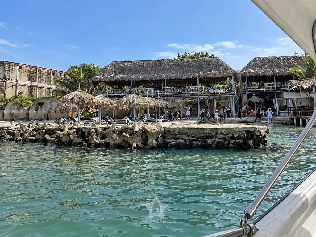 Llegada en lancha a Playa Dorada: espolón con bohíos y el club de techos de palma