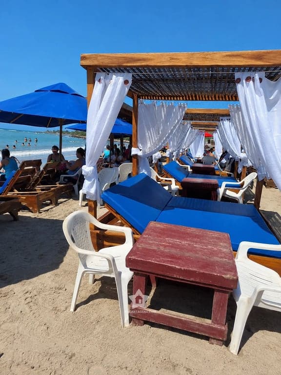 Cama con dosel junto a una sombrilla azul en la playa de Tierra Bomba, frente al mar abierto