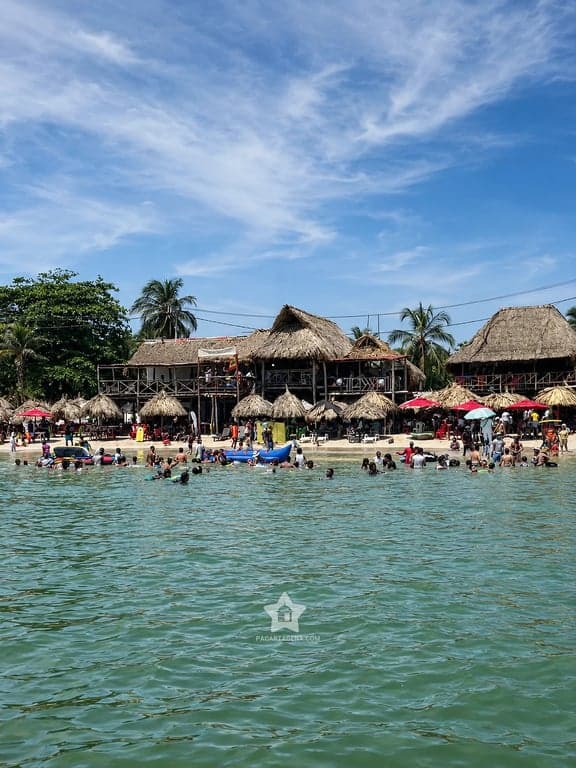 La playa de Punta Arena vista desde el agua, con sus kioscos de palma y visitantes bañándose