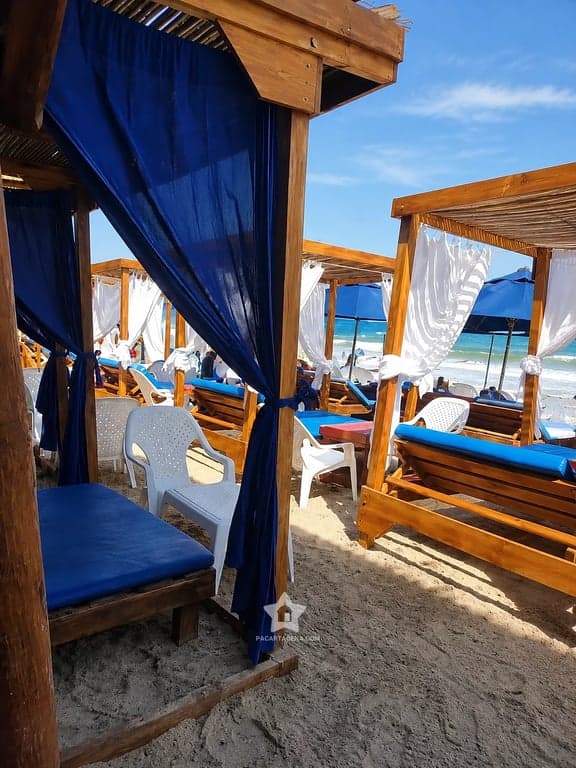 Cama con dosel y cortina azul en la arena de Playa Linda, Tierra Bomba, a pasos del agua