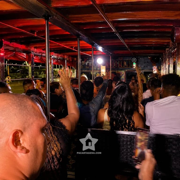 Rumba a bordo de la chiva: pasajeros bailando con las manos en alto bajo las luces de colores