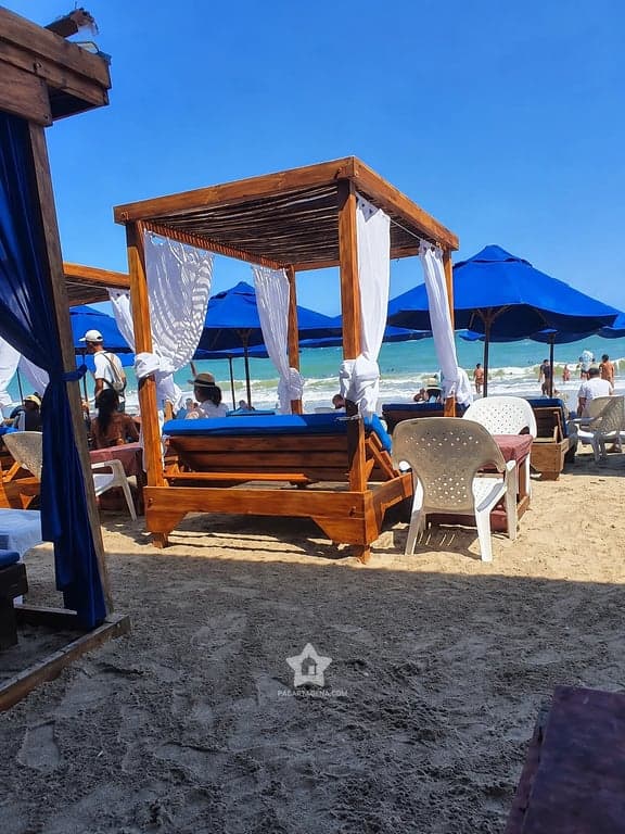 Cama con dosel y cortinas en Playa Linda, Tierra Bomba, con sombrillas azules y el mar al fondo